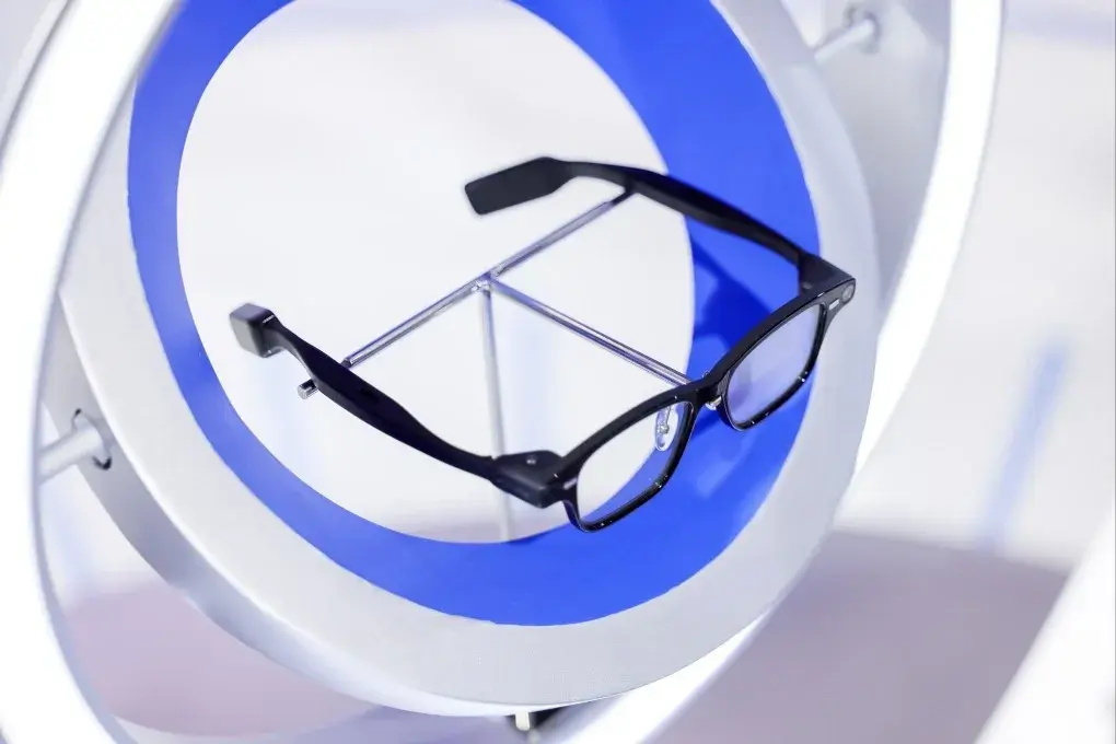 A pair of Alibaba Qwen AI Glasses are displayed on a circular, futuristic stand with a blue and white color scheme.