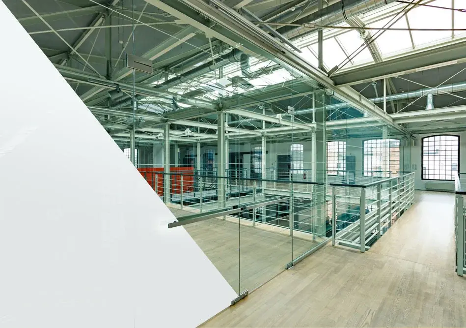 A spacious, modern indoor area featuring glass railings, exposed structural elements, large windows, and a clean, industrial design, likely part of a tech or innovation workspace showcasing DreamGlass Flow products.