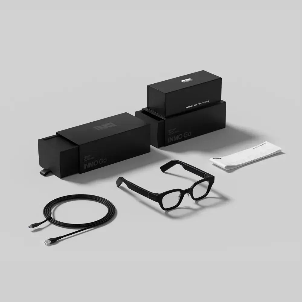 The image shows a set of black accessories, including glasses, a charging cable, a user manual, and two black boxes labeled "INMO GO," presented on a light gray surface.