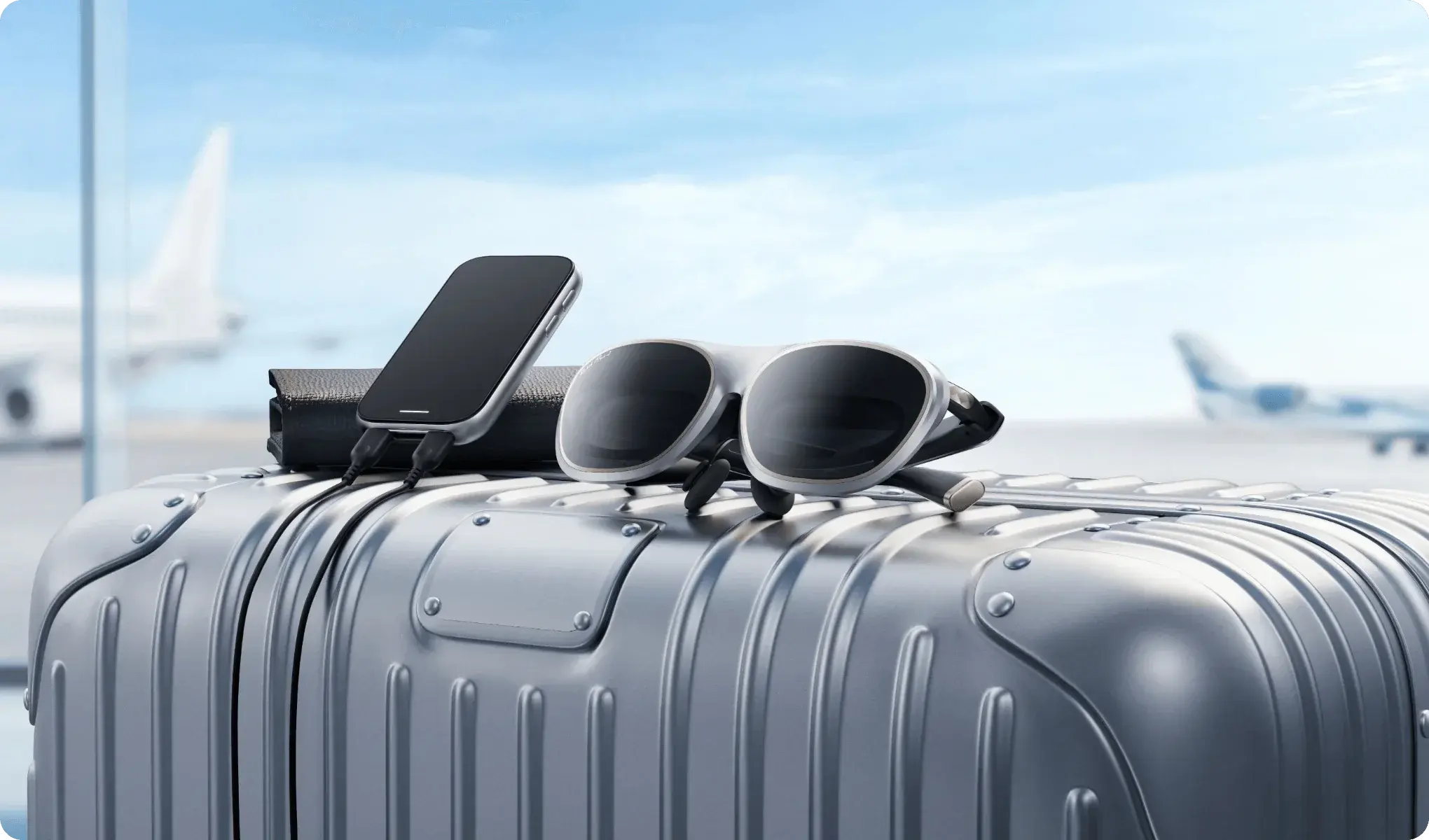 A pair of Rokid AR Lite smart glasses, a smartphone, and a charging case are placed on top of a silver suitcase in an airport setting with airplanes visible in the background.