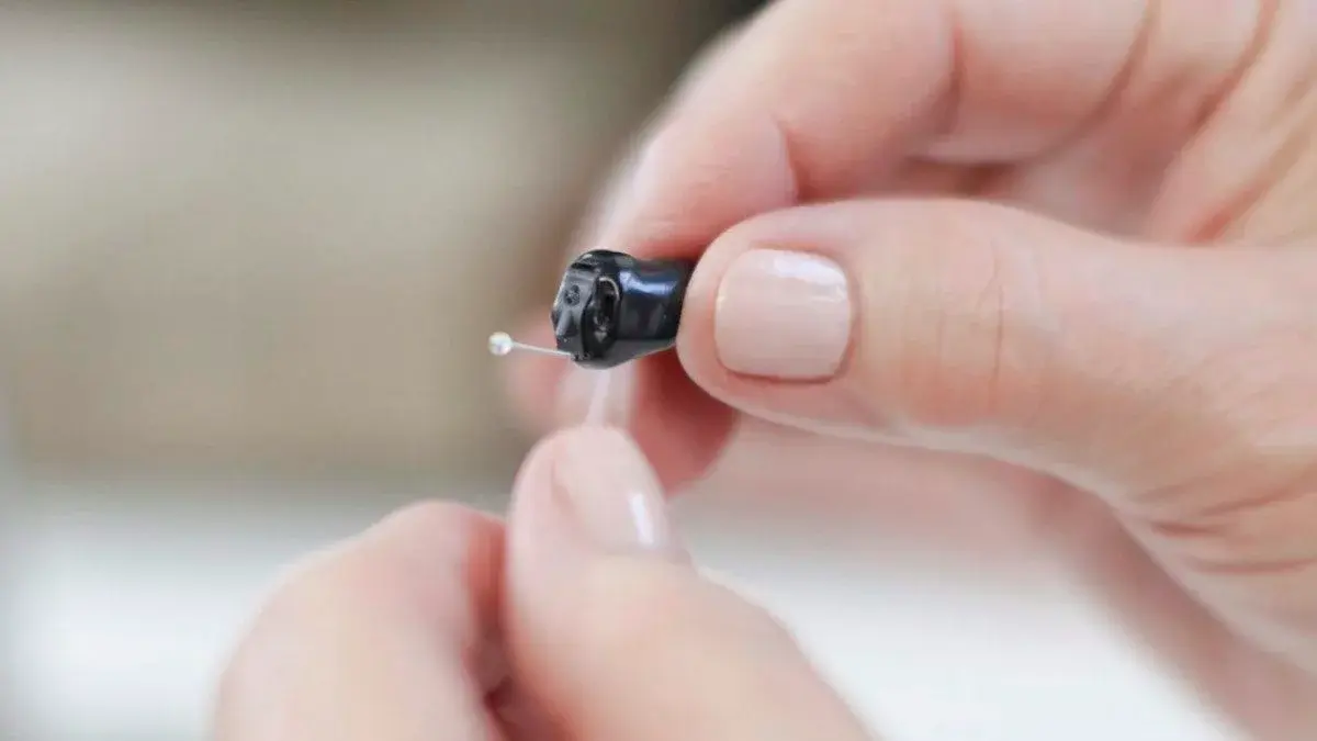 Custom CIC hearing aid resting on fingertip — invisible-fit demonstration